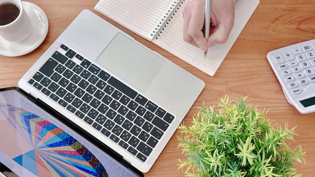 パソコンの前でノートにメモをしている画像