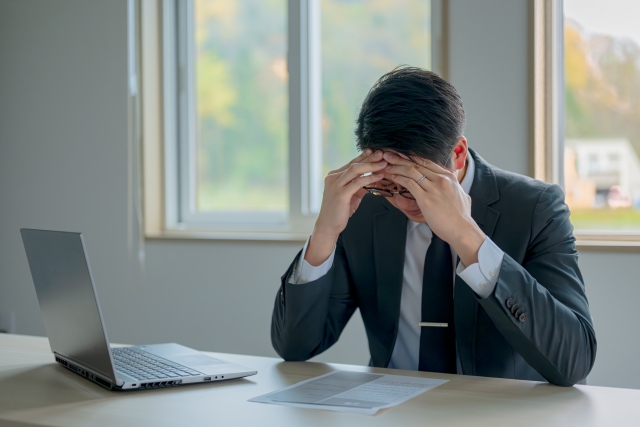 パソコンの前で頭を悩ませている人の画像