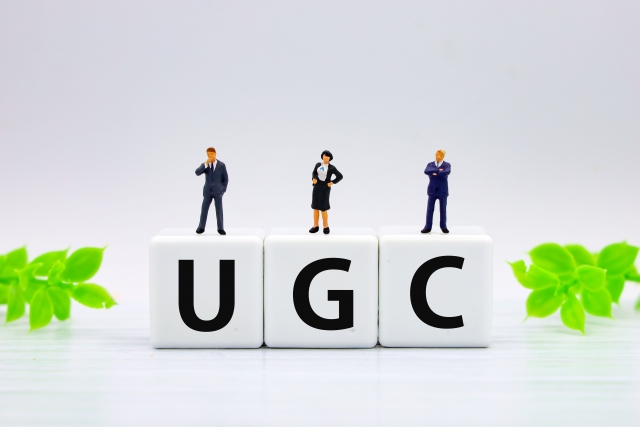 「U」「G」「C」と書かれたブロックの上に、会社員風の人形が置かれている画像