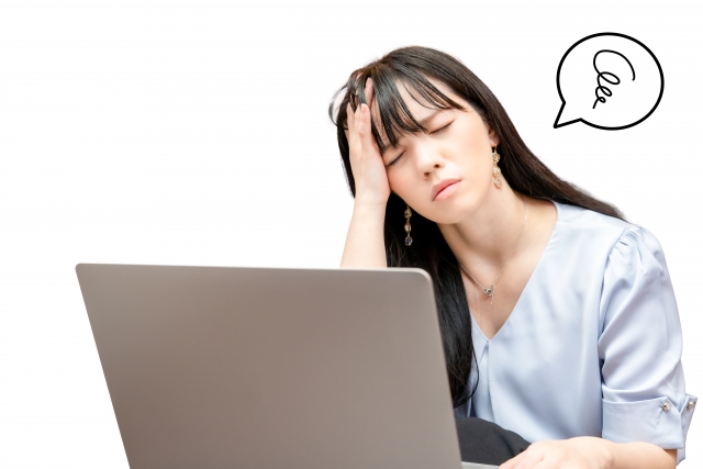 パソコンの前で頭を悩ませている人の画像