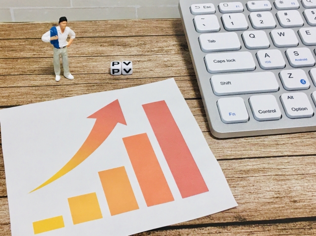 右肩上がりのグラフが印刷された紙の前に、ビジネスマン風の人形が立っている画像