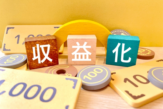 お金を模した積み木の中に、「収」「益」「化」と書かれたブロックが置かれている画像