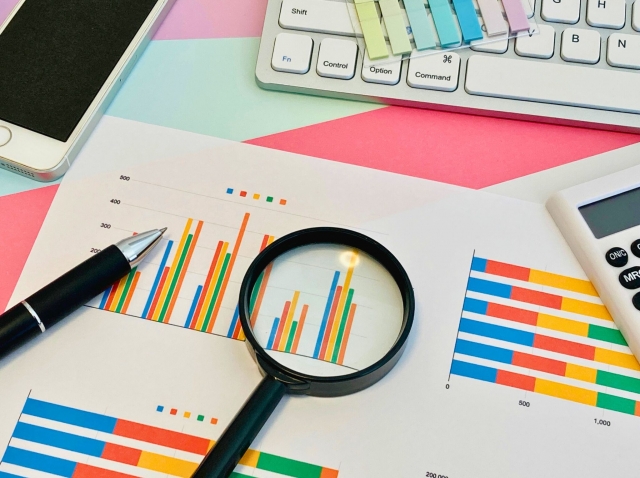 様々なグラフの上に、虫眼鏡やペンが置かれている様子の画像