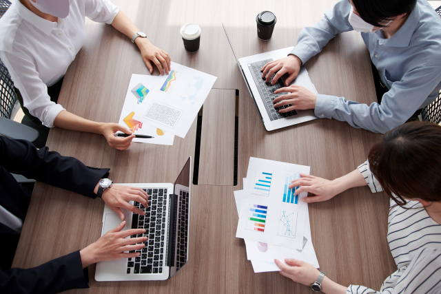 様々なグラフが印刷された資料を手に、会議をしている人たちの画像