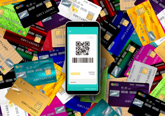 大量のクレジットカードの上に、決済用バーコードが表示されたスマートフォンが置かれている画像